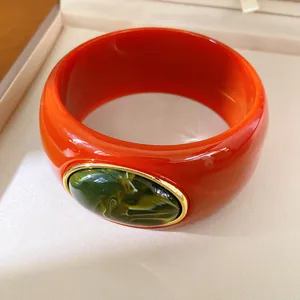 Detail of red resin bangle bracelet with green cabochon in gold frame