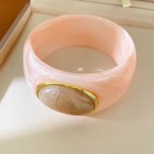 Close-up detail of a thick pink resin bangle with an oval marble-patterned stone inlay.