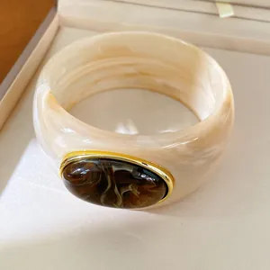 Detail view of a luxury marbled resin bangle with dark brown stone inlay in gold frame