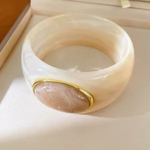 Macro view of creamy resin bangle with marble texture and elegant golden oval bezel inlay
