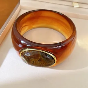 Detail view of a chunky amber resin bangle with an oval marbled stone in gold-tone setting