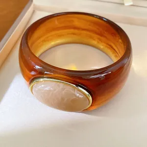 Macro detail view of a marbled amber resin bangle featuring a gold-framed stone inlay