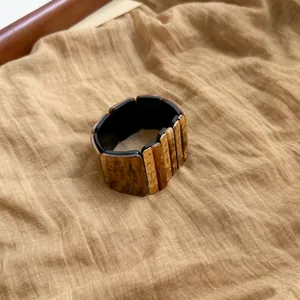 Detalle macro de pulsera elástica geométrica en ámbar y negro sobre tela de lino
