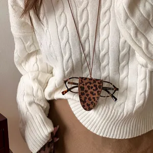 Collier porte-lunettes vintage en cuir imprimé léopard sur un pull en maille torsadée blanc.