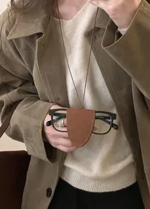Détail d'un collier porte-lunettes en cuir marron vintage porté sur un pull neutre