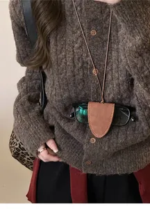 Détail d'un collier porte-lunettes en cuir vintage porté sur un pull en maille marron