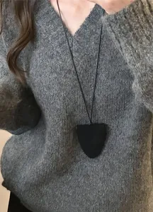 Gros plan d'un collier en cuir noir minimaliste et porte-lunettes sur un pull gris