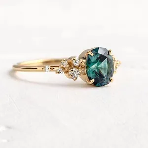 Vista dettagliata di un anello in oro con pietra preziosa verde acqua ovale e diamanti.