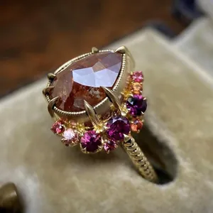 Close-up of a vintage-style gold ring with a pear-shaped orange zircon and pink stones
