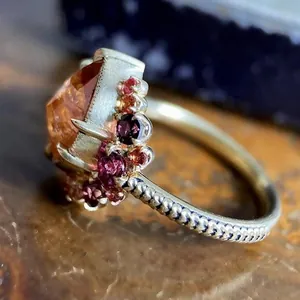 Close-up of boho style engagement ring with orange and red gemstones and textured band.