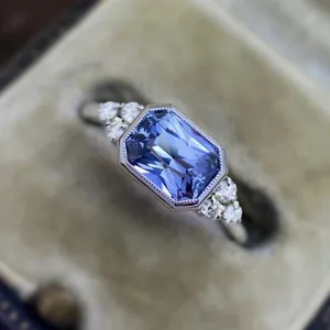 Macro detail of an emerald-cut blue zircon ring with milgrain bezel and side stones