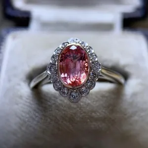 Close-up view of a vintage engagement ring featuring a pink oval zircon with halo setting