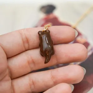 Detailed handheld view of a cute brown glossy animal charm pendant with gold chain loop