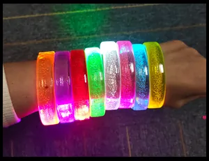 Detail view of various colorful LED flashing acrylic bracelets glowing on a human arm.