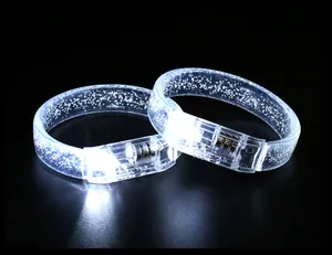 Detail view of two glowing white LED acrylic glitter bracelets on a dark background