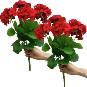 Vibrant red artificial geranium flowers with green leaves held against a white backdrop.
