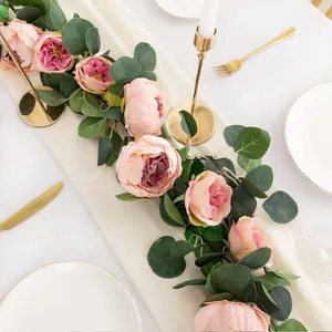 Close-up of artificial pink peony and eucalyptus leaf garland on a white wedding table.