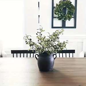 Artificial olive branches with fruits in a dark pot on a wooden dining table
