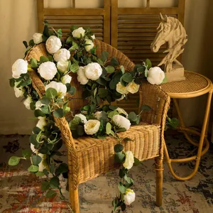 Artificial white peony and eucalyptus leaf vine draped elegantly over a vintage wicker chair