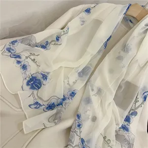 Close-up detail view of a sheer white chiffon scarf with elegant blue floral prints