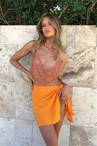 Detalle de top halter de malla con pedrería y espalda descubierta con falda cruzada naranja