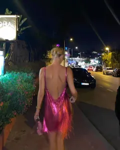 Nighttime back view of a woman in a hot pink metallic sequin backless tassel dress