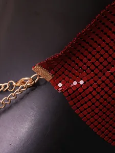 Close-up detail of red metal mesh sequins and golden chain strap of a halter top