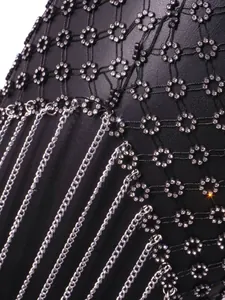 Detailed macro view showing sparkling rhinestone flowers and silver chain tassels on black mesh dress