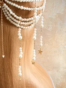 Close-up detail of a multi-strand white pearl body chain with elegant golden charms