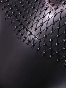 Macro view of sparkly rhinestones embedded in black fishnet mesh fabric for a sexy top.