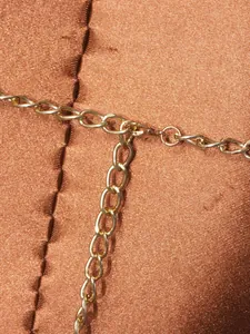 Dettaglio squisito di una catena per il corpo in metallo dorato su tessuto di raso marrone