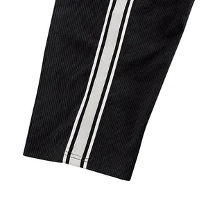 Detailansicht einer schwarzen Cordhose mit weißen Seitenstreifen und Rippstruktur.