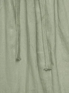 Primo piano del tessuto in misto lino e dei cordoncini dei pantaloni verde salvia.