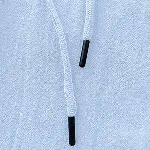 Close-up detail of a white braided drawstring with black tips on light blue linen pants