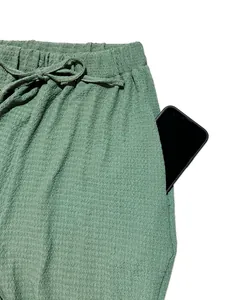 Close-up detail of green textured pants featuring a functional side pocket and drawstring