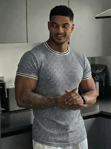 Model wearing a grey ribbed athletic T-shirt with contrast trim in a modern kitchen.