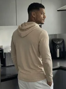 Back view of a men's lightweight beige hooded long sleeve t-shirt in a kitchen setting.