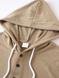 Close-up of khaki hoodie neckline with black buttons and white drawstring detail.