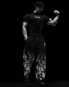 Männliches Model in schwarzem Kompressionsshirt und Gothic-Print-Jogginghose mit Muskeldefinition
