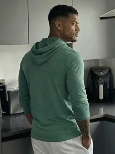Back view of a green heathered hoodie showing texture and hood design in a kitchen
