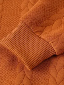 Primo piano del maglione da uomo arancione con trama jacquard e dettagli dei polsini a coste.