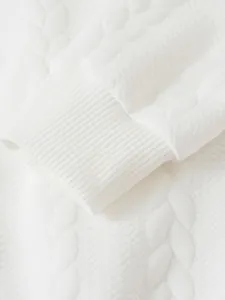 Dettaglio di un maglione bianco da uomo con polsini a costine e motivo a treccia