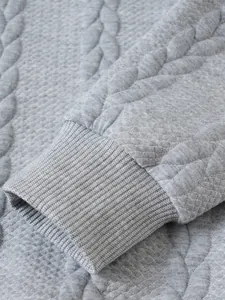 Dettaglio del polsino a coste e della trama a treccia strutturata di un maglione grigio