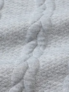 Dettaglio ravvicinato della trama a treccia grigia e del motivo jacquard di un maglione da uomo