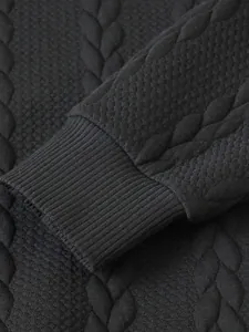 Dettaglio di un maglione a trecce nero che mostra il polsino a coste e il tessuto
