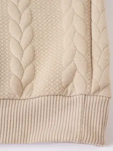 Vista macro di un maglione beige con motivi a treccia e jacquard a diamante.