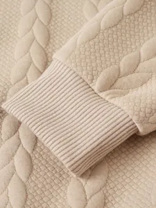 Vista ravvicinata che mostra il polsino a costine e la trama a trecce di un maglione beige