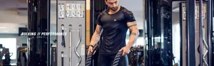 Muscular man in black high-elasticity compression gym t-shirt training with battle ropes in gym