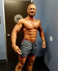 Hombre atlético posando en gimnasio con shorts deportivos grises de malla y borde rojo