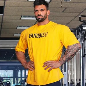 Gespierde man in de sportschool met oversized geel katoenen fitness shirt met Vanquish-logo